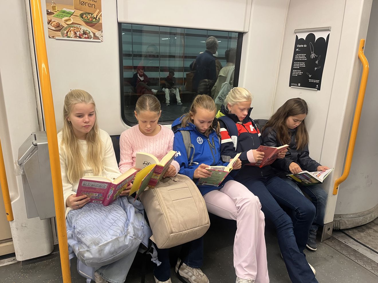 en gruppe barn som sitter på t-banen og leser bøker
